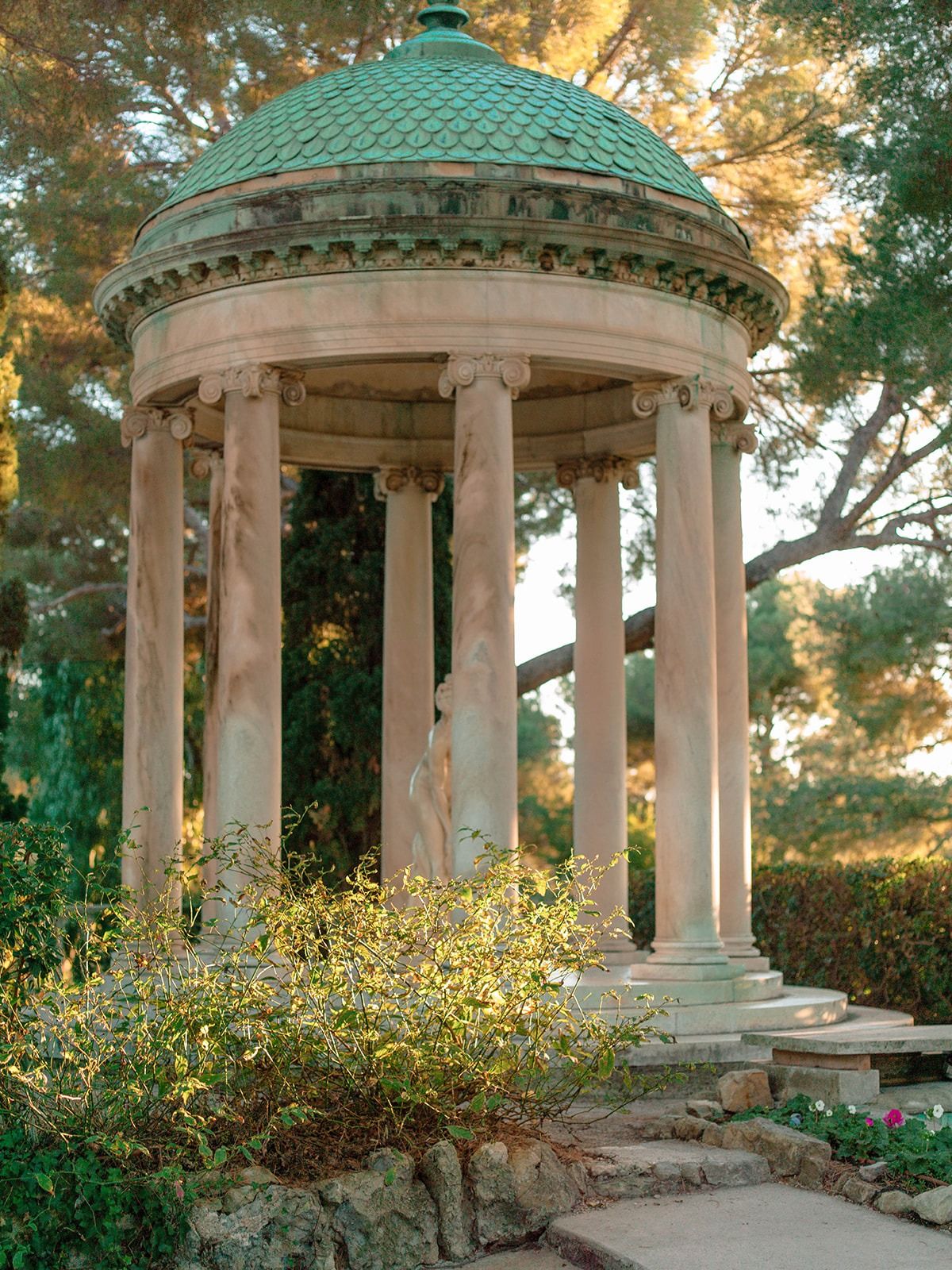 Classical circular pavilion with columns and a green roof in the villa gardens